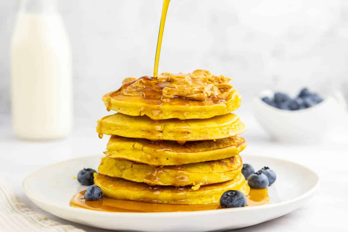 protein pancakes without protein powder stacked on a plate with blueberries, peanut butter and maple syrup