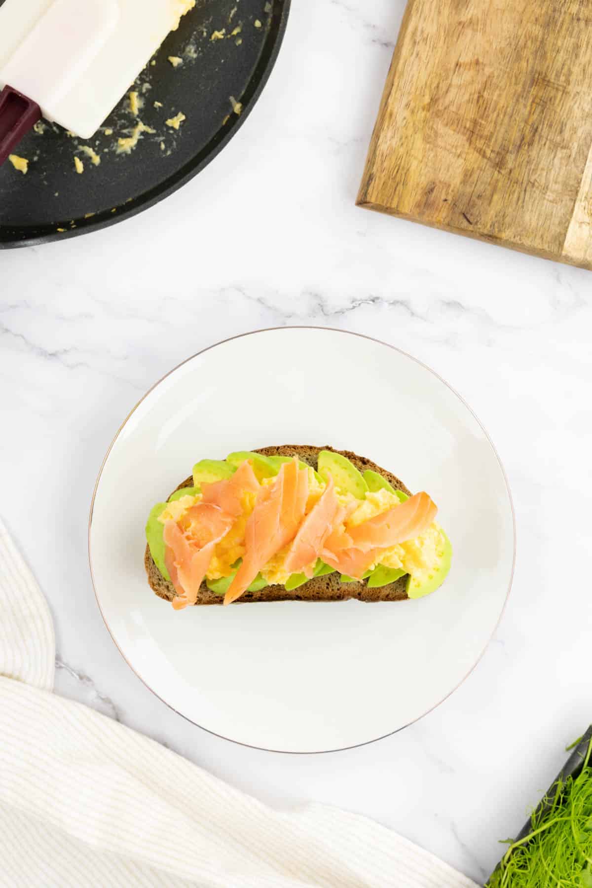 Sliced avocado on toast topped with scrambled eggs and smoked salmon