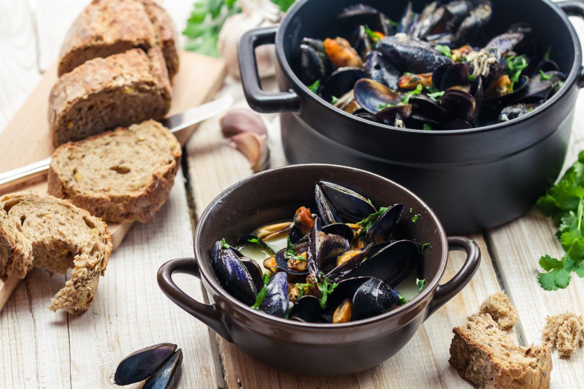 20 Highest Protein Fish and Seafood 10 A pot of mussels cooked in a garlic and herb sauce, served with bread.