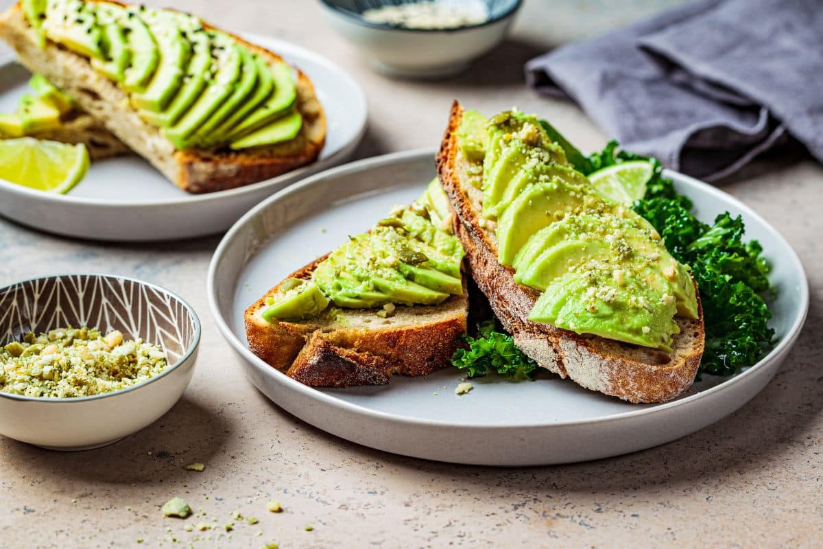 Sliced avocado on toast with nuts and a lime wedge.