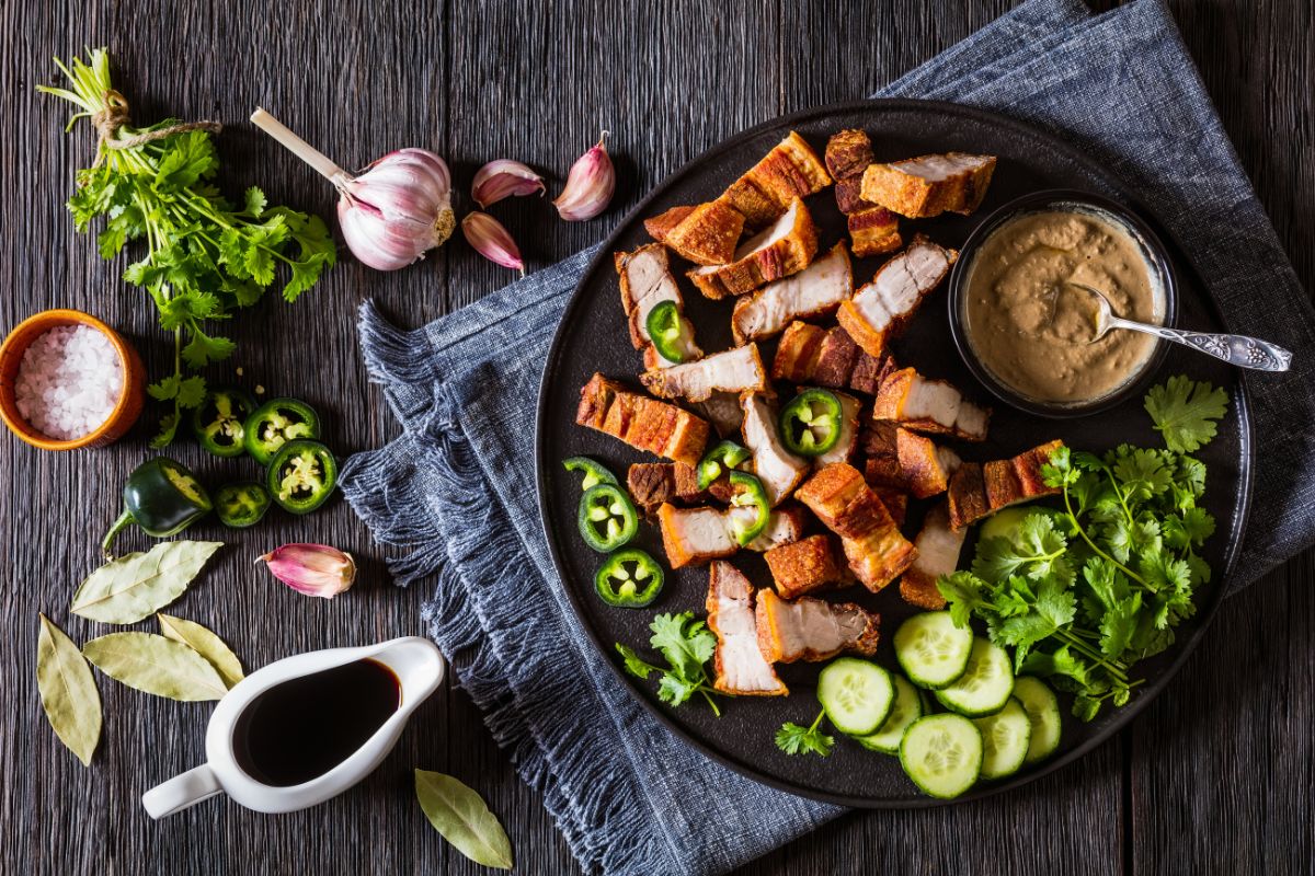 20 Highest Calorie Meats for Weight Gain 2 Crispy pork belly on a plate with vegetables and a dip.
