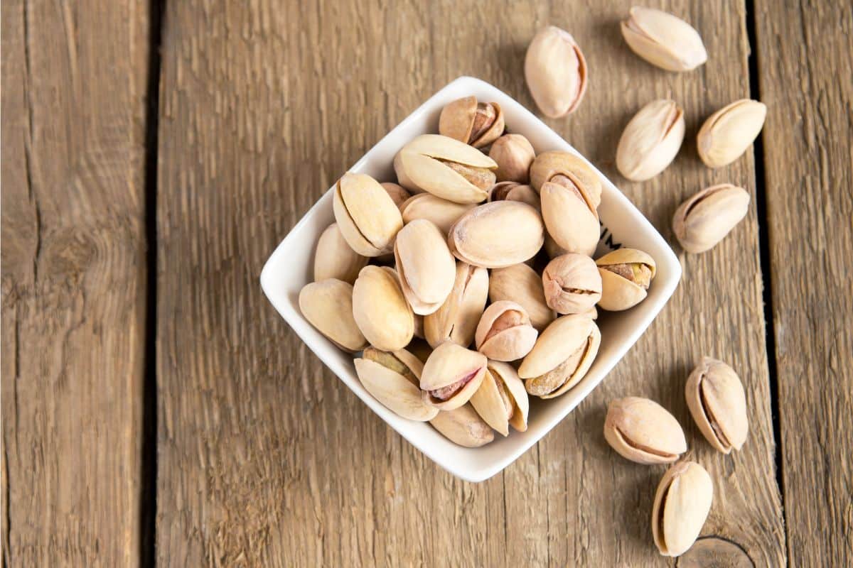 The Top 10 Highest Protein Nuts 4 Pistachios in a bowl and on a wooden table.