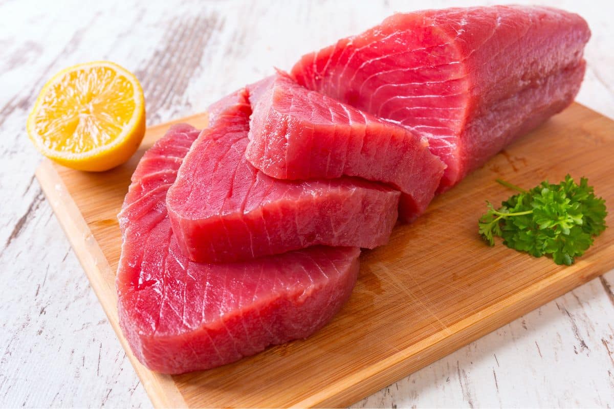 Tuna steak sliced on a wooden board with lemon.