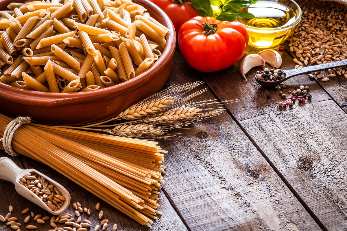 Wholegrain penne and wholegrain spaghetti on a board next to extra virgin olive oil.